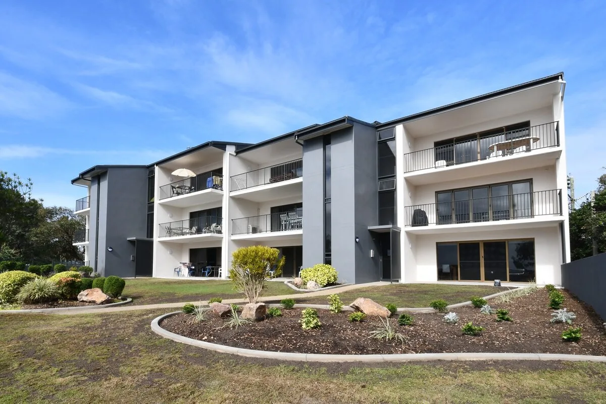 A modern apartment building with balconies overlooks landscaped grounds.