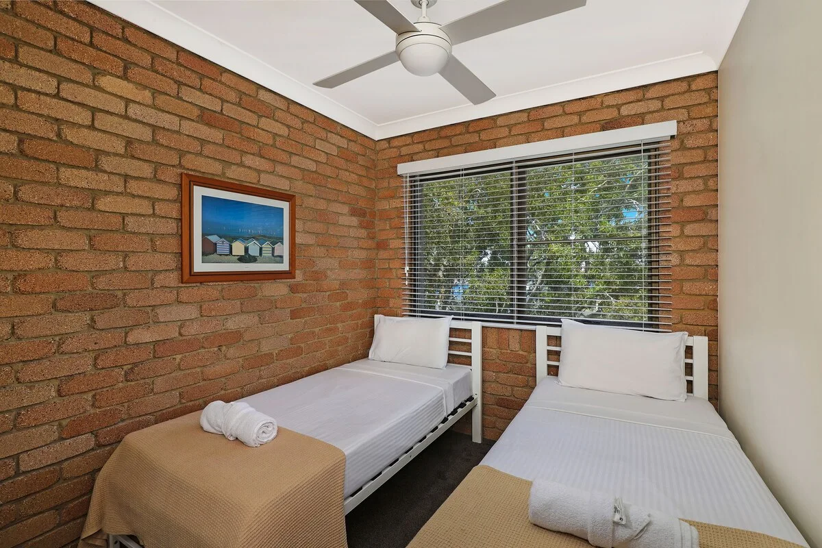 A bedroom with two single beds, a window, and exposed brick walls.