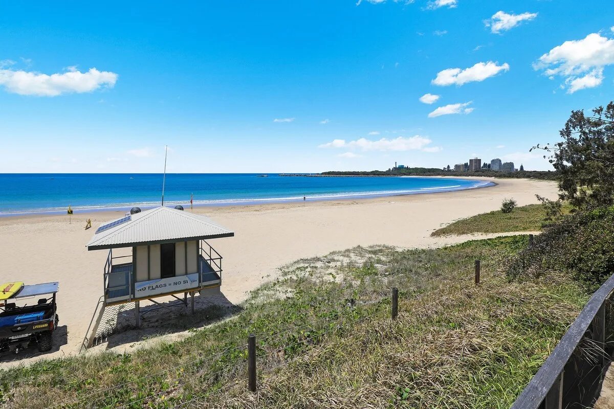 A sandy beach curves beside calm blue water under a bright sky.
