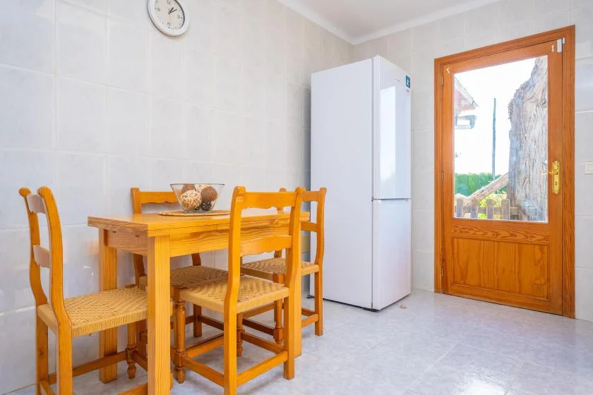 Comedor con una mesa y sillas de madera junto a un refrigerador y una puerta de vidrio.