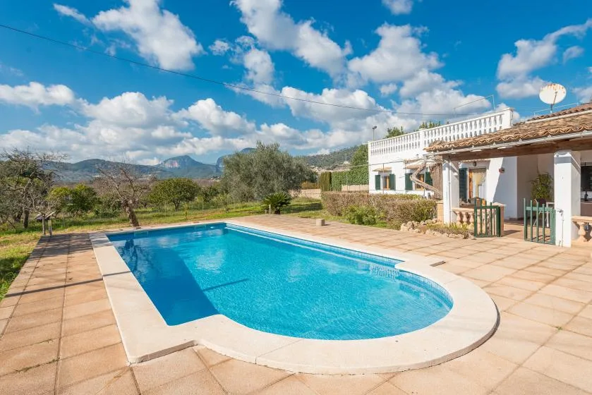 Una piscina al aire libre junto a un edificio blanco y un patio embaldosado.