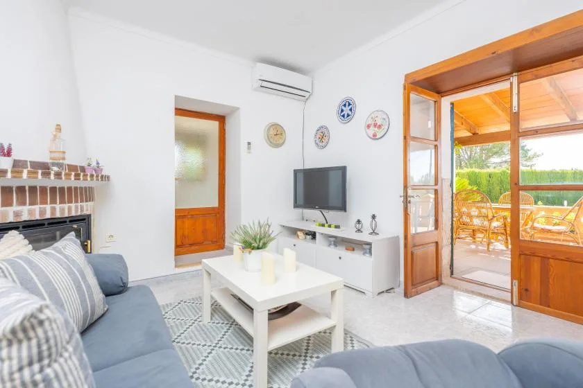 Una sala luminosa con asientos, un televisor y puertas que dan a una zona exterior cubierta.