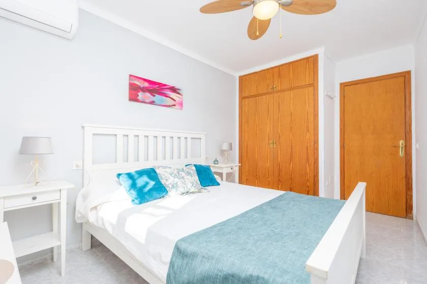Dormitorio luminoso con una cama blanca, ropa de cama turquesa y puertas de madera.