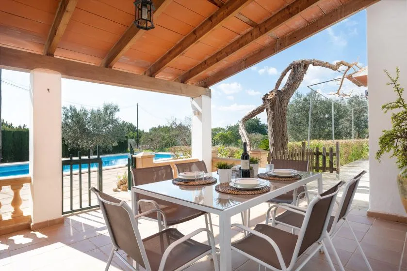 Comedor exterior cubierto con mesa y asientos junto a una piscina.