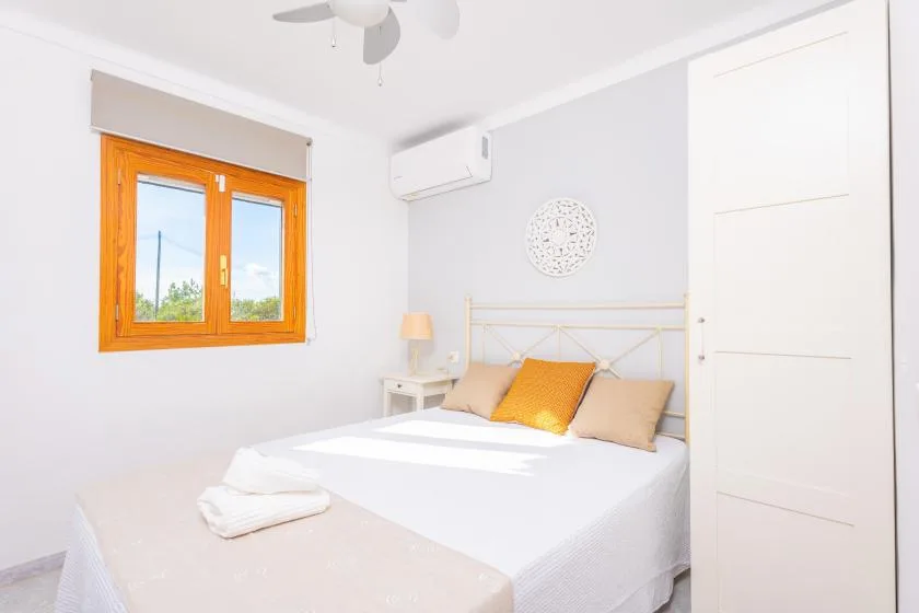 Un dormitorio luminoso con una cama bajo un adorno de pared y una ventana con marco naranja.