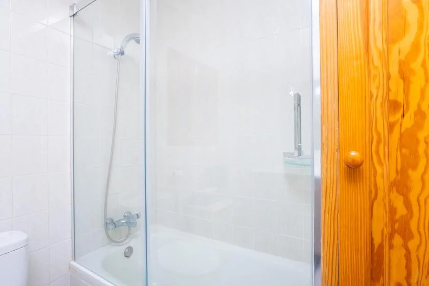 Un baño alicatado con una ducha de vidrio y una puerta de madera.