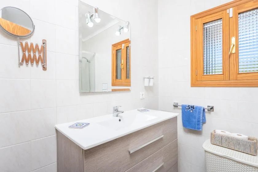 Un baño luminoso con una amplia encimera de lavabo y una ventana con marco de madera.