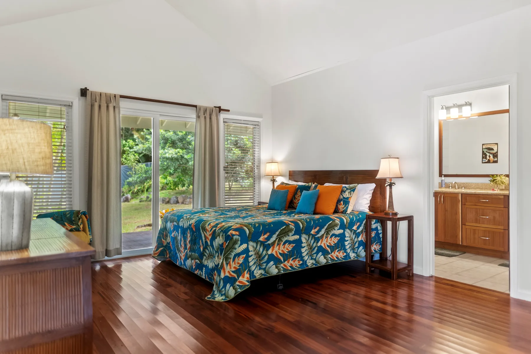 Un dormitorio con una cama cubierta con una colcha azul de flores junto a grandes ventanas.
