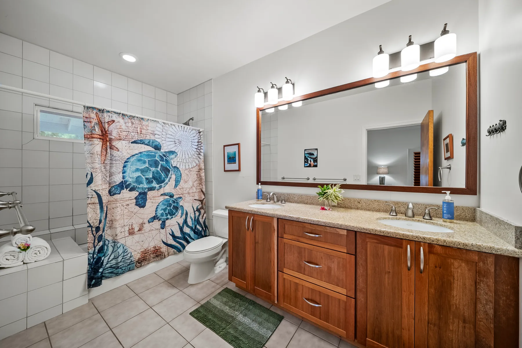 Un baño alicatado con tocador de madera, espejo grande y cortina de ducha colorida.