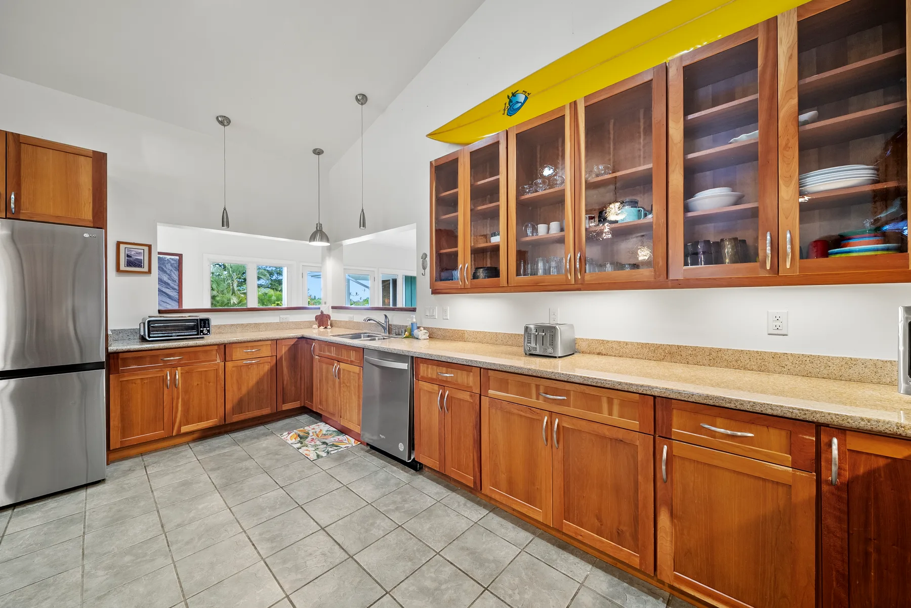 Una cocina con gabinetes de madera, piso de baldosas y ventanas sobre la encimera.