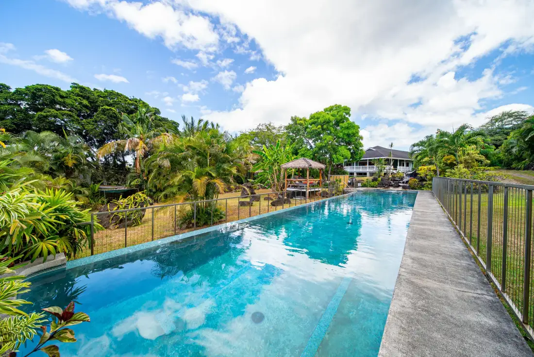 Una piscina al aire libre junto a un camino pavimentado y abundante vegetación tropical.