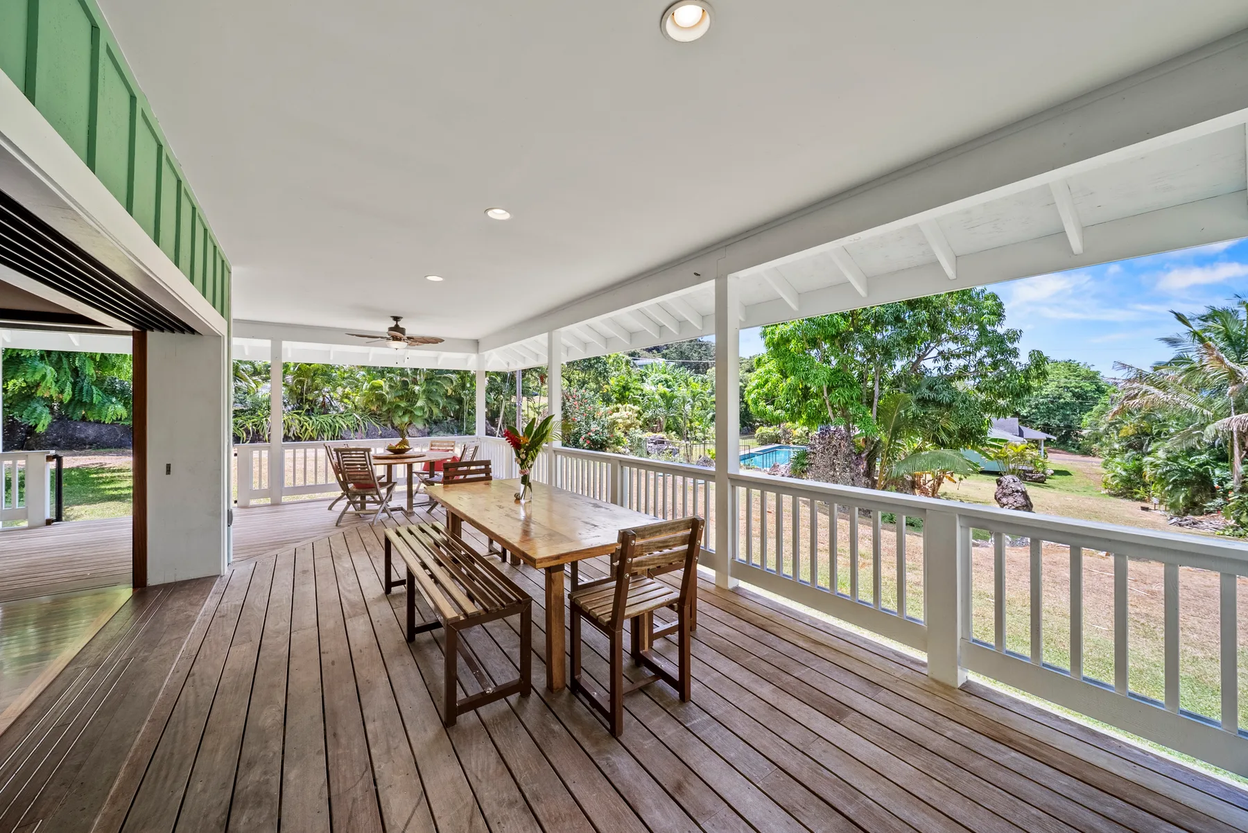 Una zona de comedor exterior cubierta con una mesa larga de madera y vistas al jardín.