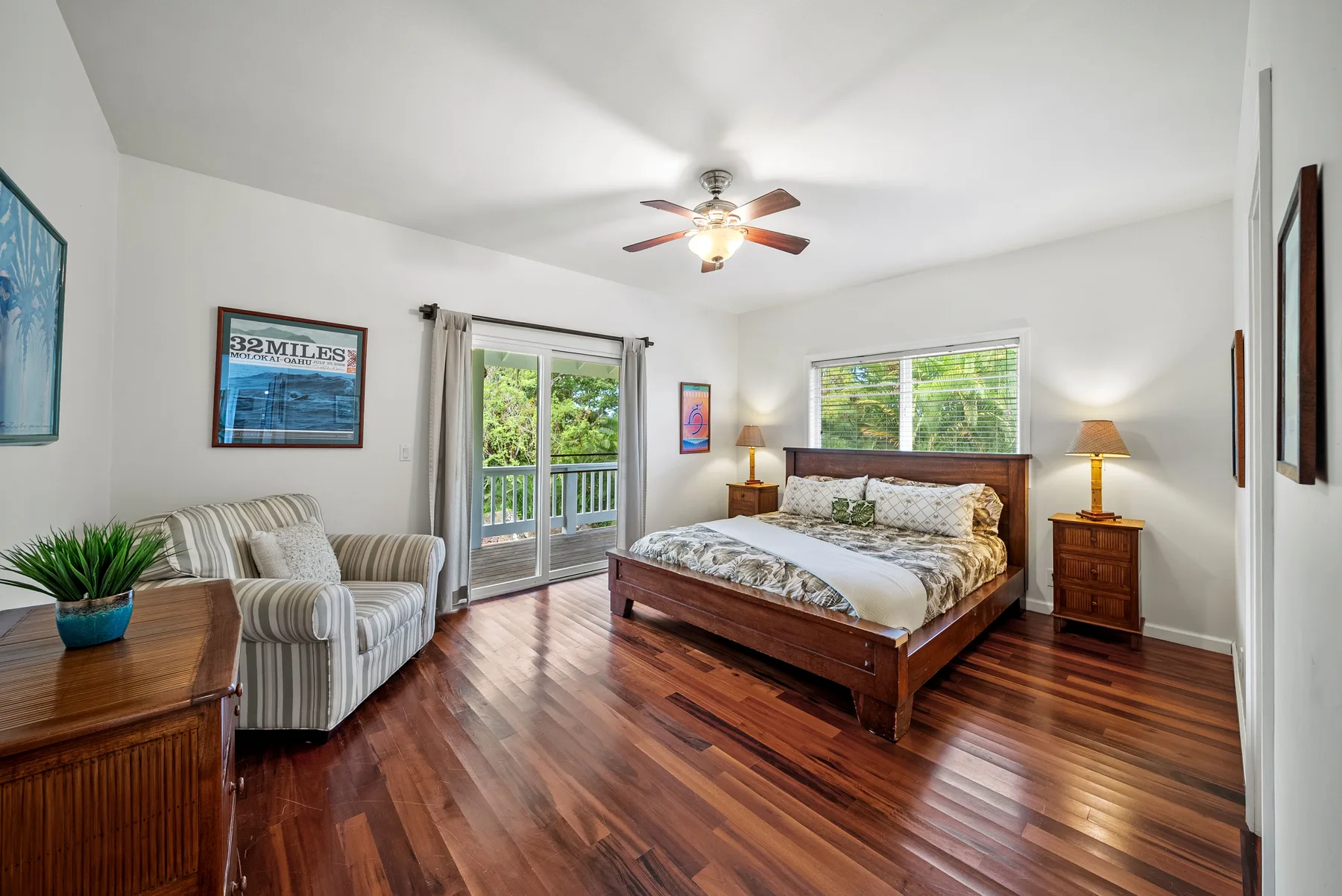Un dormitorio luminoso con cama de madera, asientos a rayas y puertas de vidrio hacia un balcón.