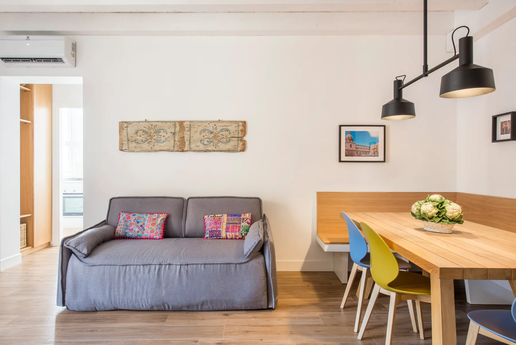 A bright living and dining area with a sofa beside a wooden table and colorful chairs.