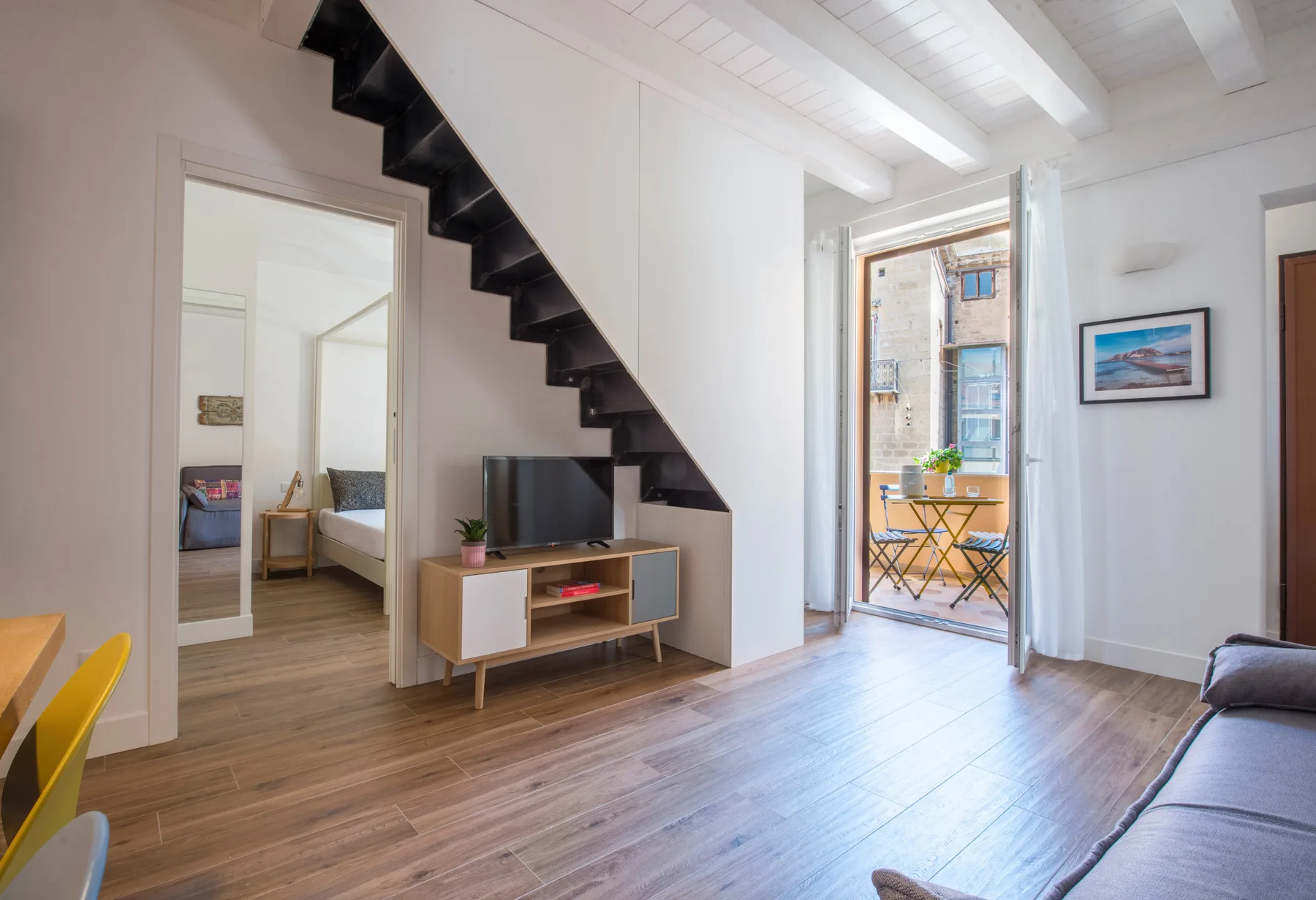 A bright living area with a television beneath a staircase and an open balcony door.