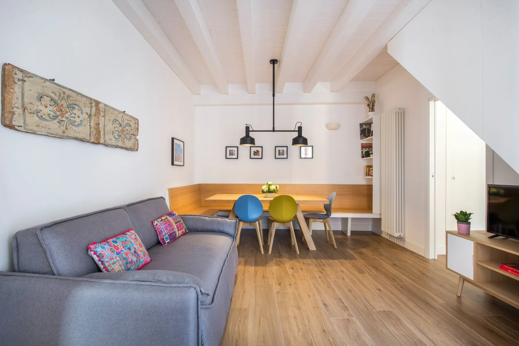 A bright living and dining area features a gray sofa and a wooden dining table.