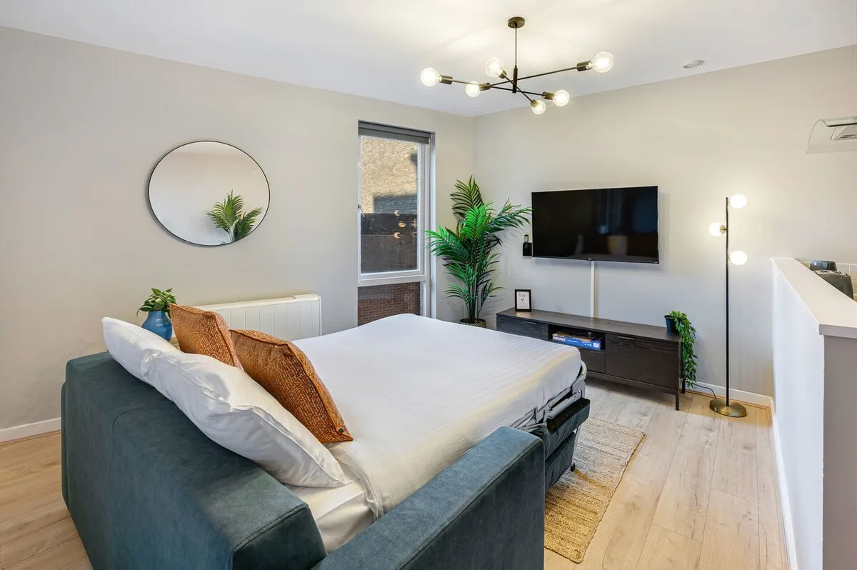 Dormitorio con una cama, un televisor montado en la pared y una lámpara de pie.