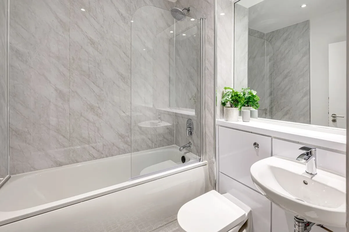 Un baño luminoso con bañera, mampara de vidrio y lavabo.