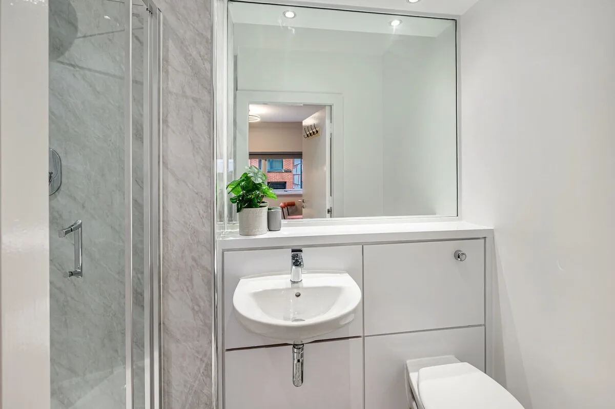 Un baño luminoso con lavabo, espejo y ducha.