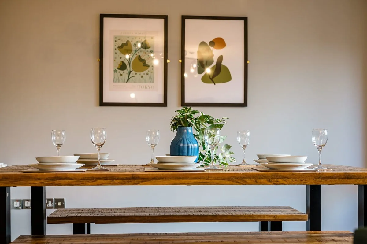 Una mesa de comedor está puesta con platos, copas y cuadros en la pared.