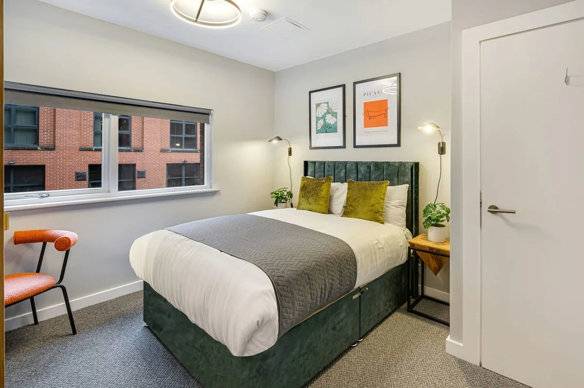 Un dormitorio con una cama, un cabecero verde y una ventana grande.