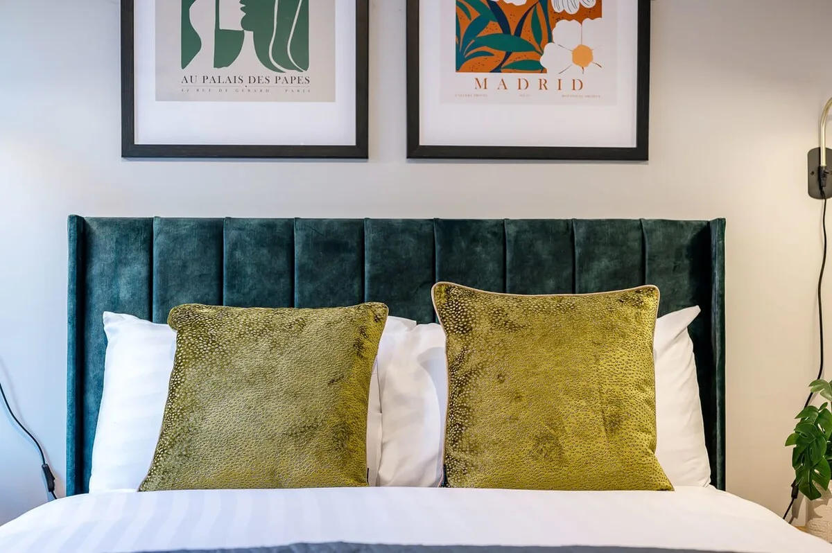 Un dormitorio con cama, cabecero tapizado verde y cojines decorativos.