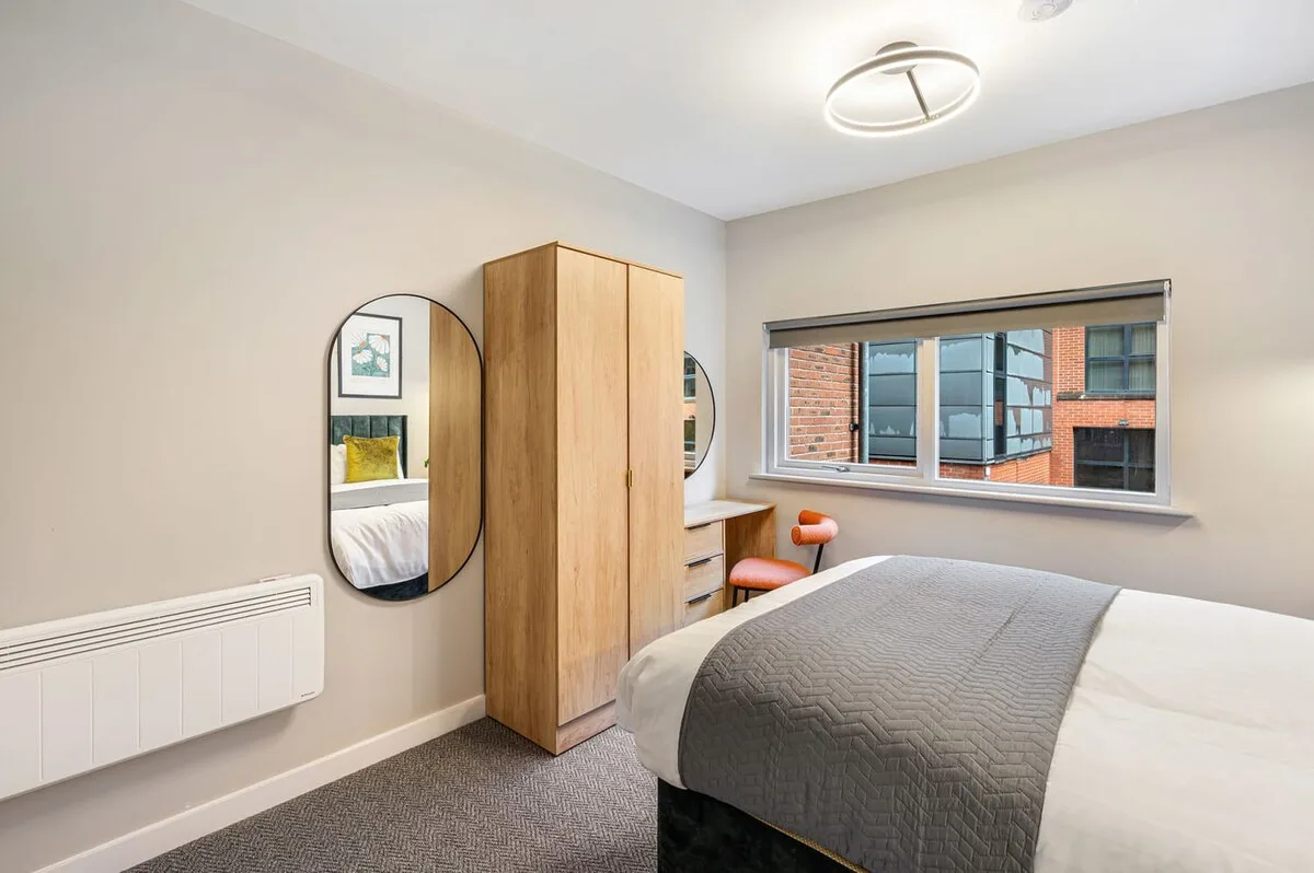 Un dormitorio luminoso con cama, armario de madera y una ventana grande.