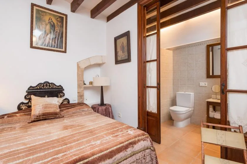 A bedroom with a bed beside an open doorway to a tiled bathroom.