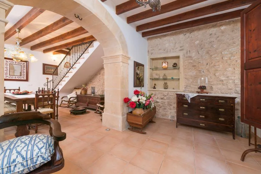 A rustic interior with a dining area, staircase, and stone walls.