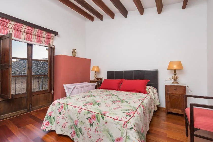 A bedroom with a floral bedspread and wooden ceiling beams.