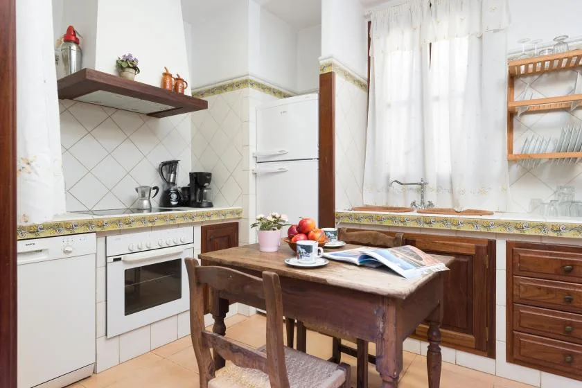 Una cocina con azulejos, una mesa de madera y electrodomésticos sobre la encimera.
