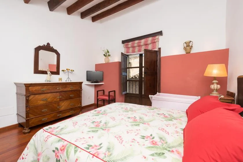 A bedroom with a floral bedspread, wooden dresser, and exposed ceiling beams.