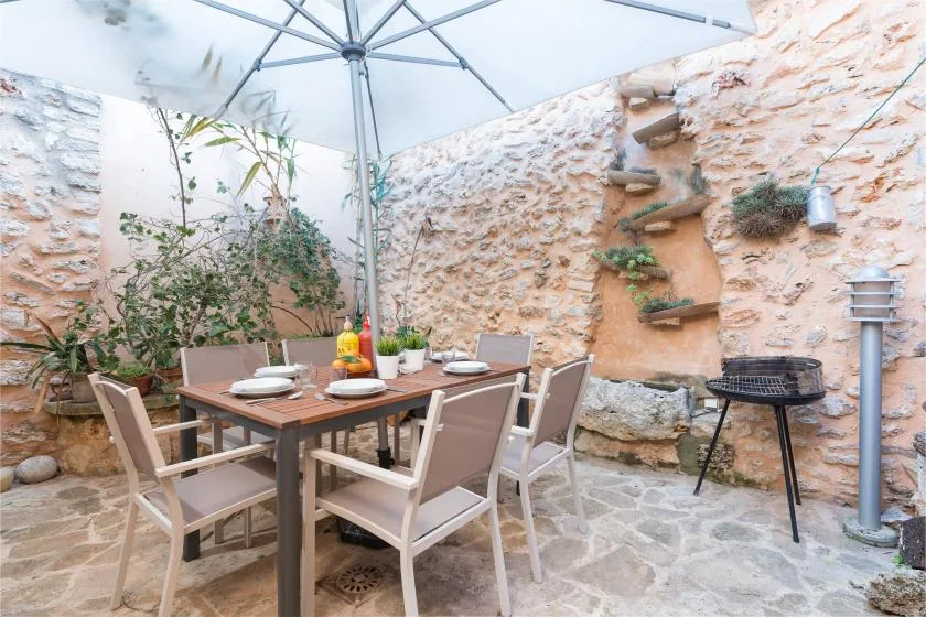 Un comedor en un patio de piedra tiene una mesa y asientos bajo una sombrilla grande.