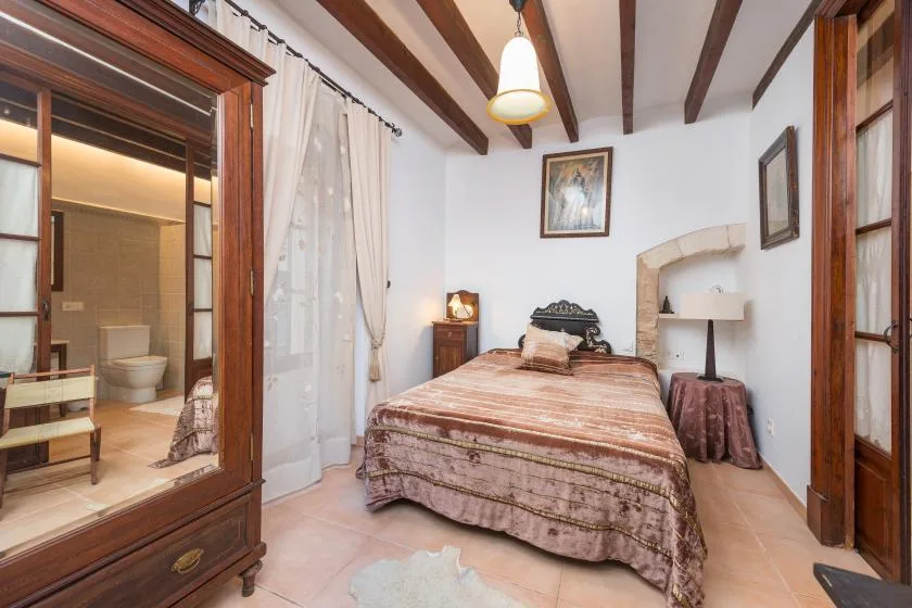 A bedroom with a double bed, framed artwork, and an adjoining bathroom visible through a doorway.