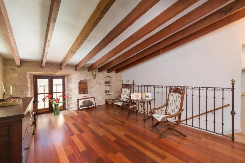 A bright living area with exposed wooden ceiling beams, polished flooring, and seating by a railing.