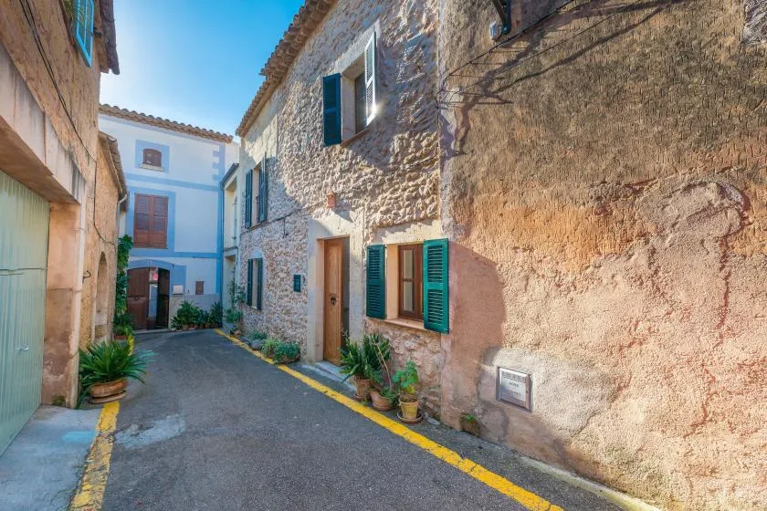 A narrow paved lane runs between stone and stucco buildings with shuttered windows.