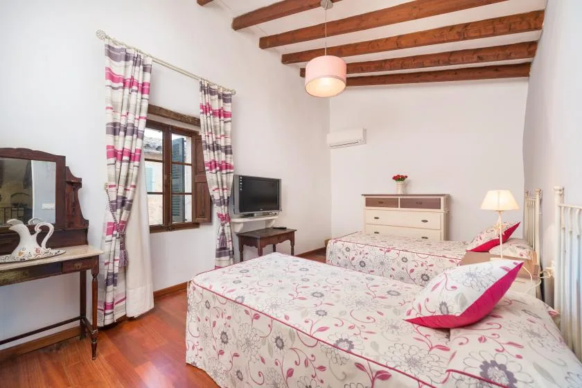 A bedroom with patterned bedding, a wooden window, and exposed ceiling beams.