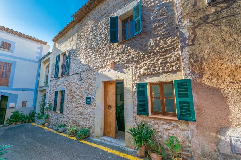 A stone building exterior with green shutters and a wooden entrance door.