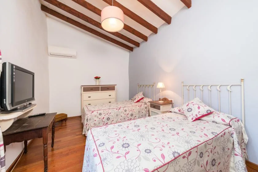 A bedroom with floral bedding, white metal bed frames, and exposed wooden ceiling beams.