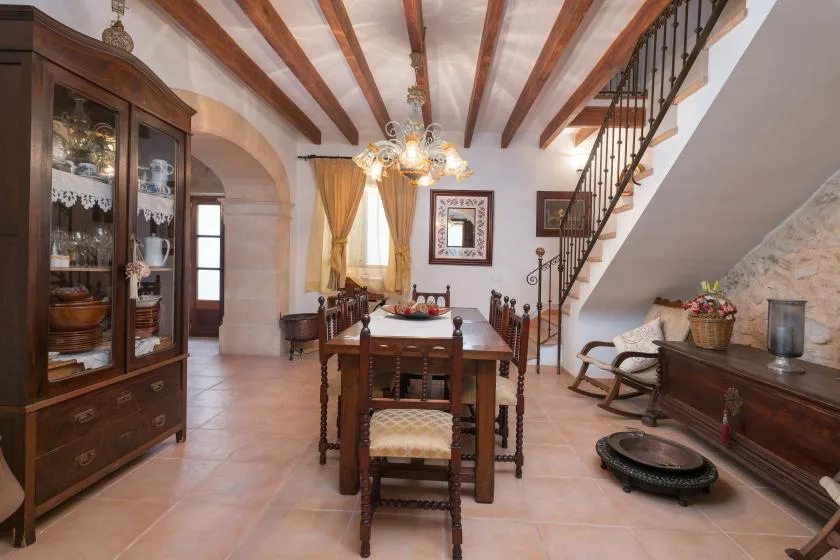 A dining room with a wooden table beneath exposed ceiling beams and a staircase.
