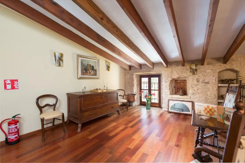 A rustic living room with exposed ceiling beams, wooden furnishings, and a stone fireplace.
