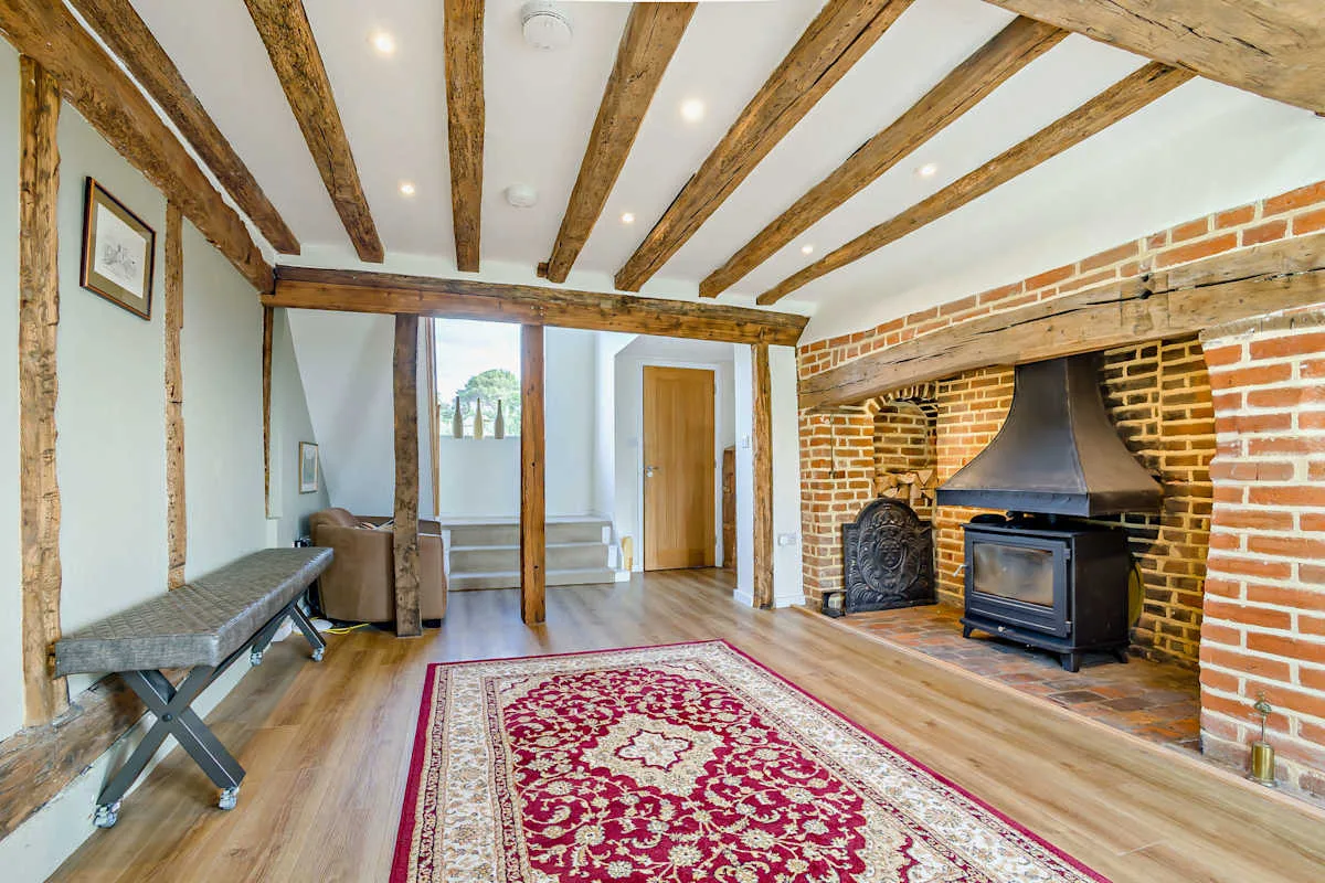 A timber-beamed living room with a brick fireplace and patterned rug.