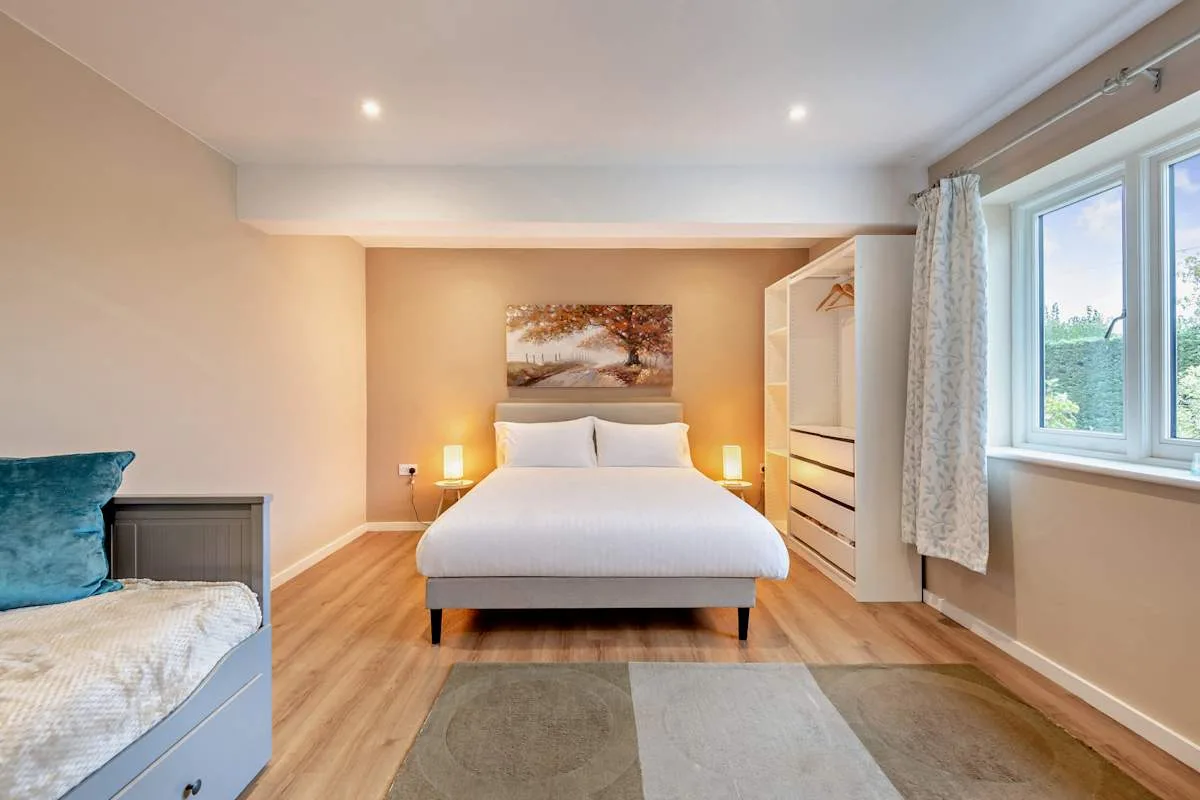 A bedroom with a double bed, a wardrobe, and windows overlooking greenery.