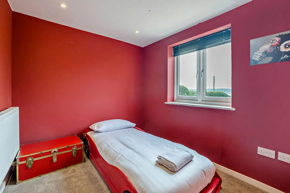 A bedroom with a single bed, red walls, and a window.