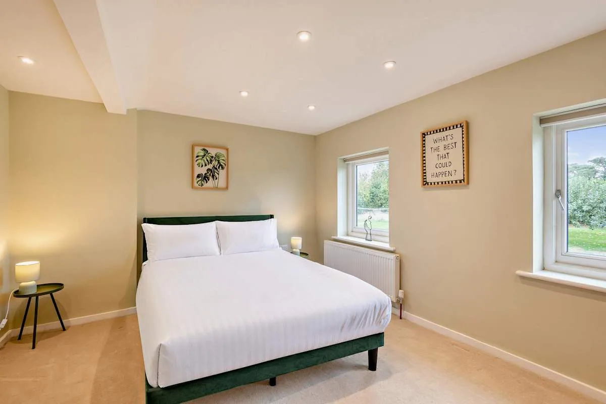 A bright bedroom with a neatly made bed and two windows.