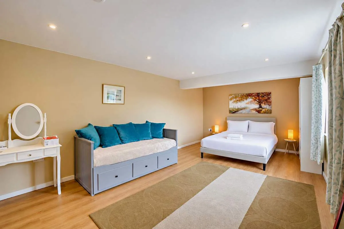A bedroom with a bed, a blue-cushioned daybed, and a rug.