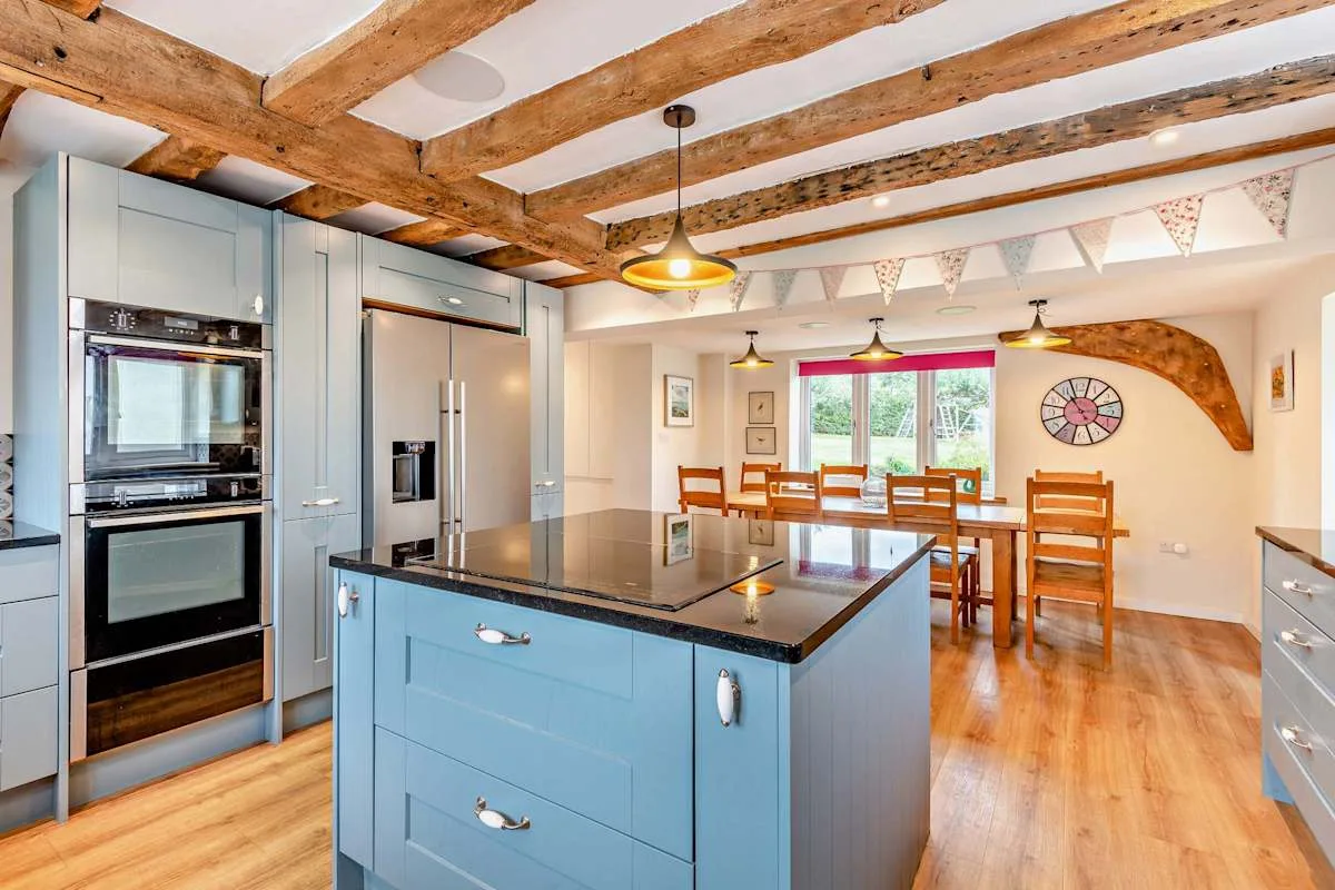A bright kitchen and dining area with a central island and wooden ceiling beams.