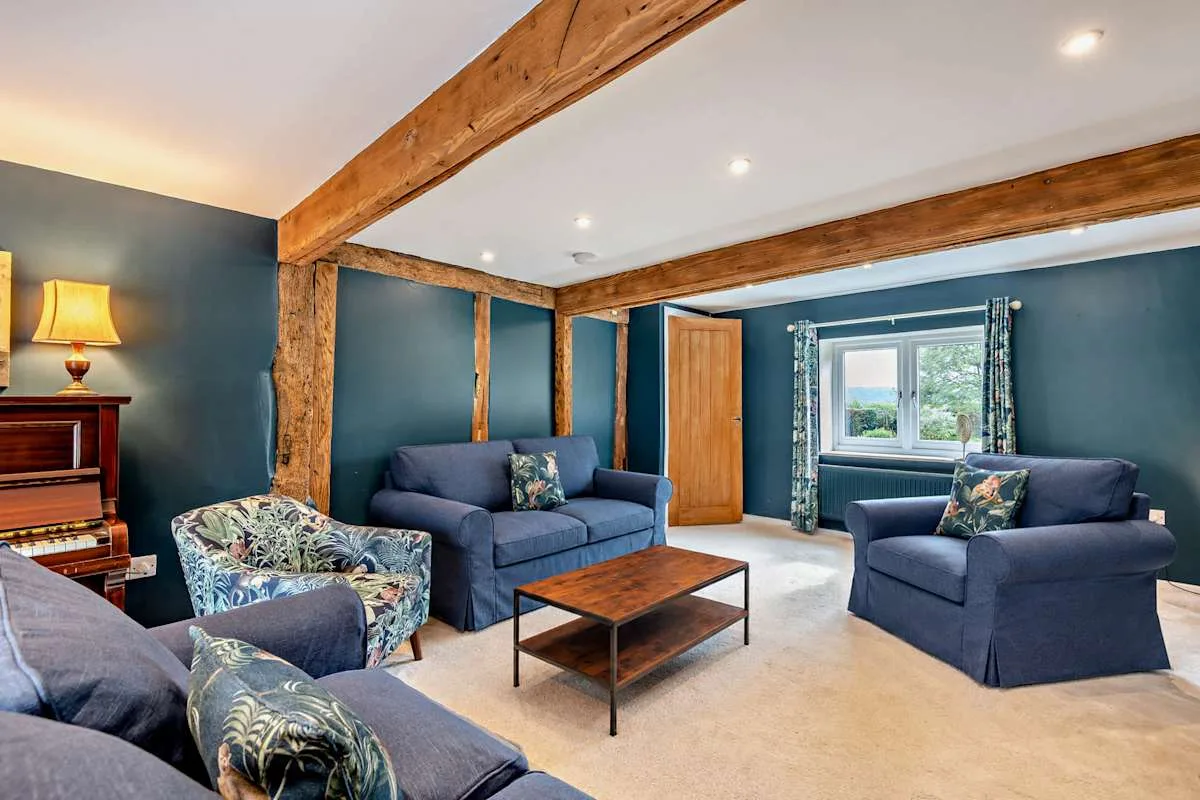A living room with blue seating, a piano, and exposed wooden beams.