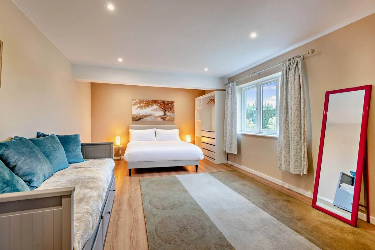 A bedroom with a bed, a seating area, and a large window.