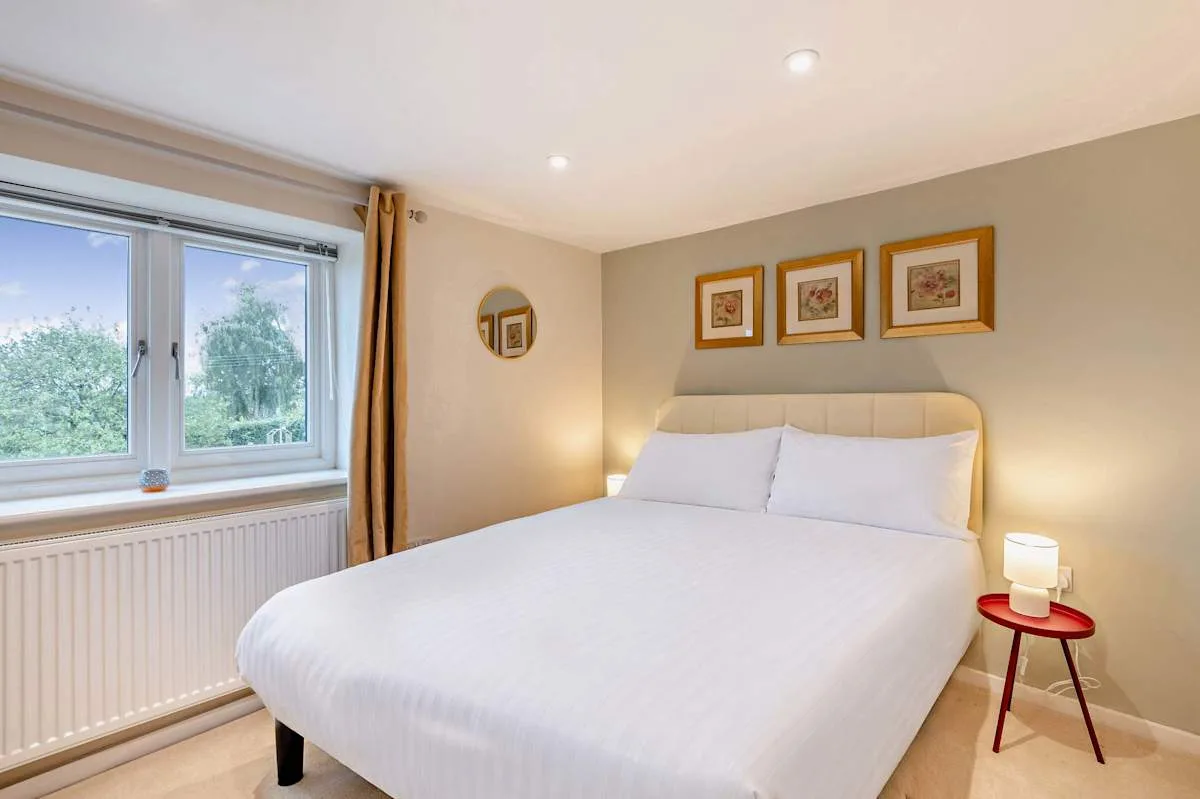 A bedroom with a neatly made bed, framed artwork, and a large window.